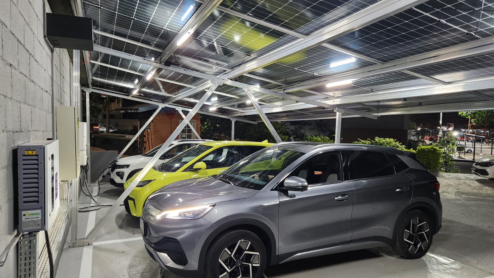 Dois veículos elétricos recarregando sob a cobertura solar do eletroposto DayBack Charger à noite